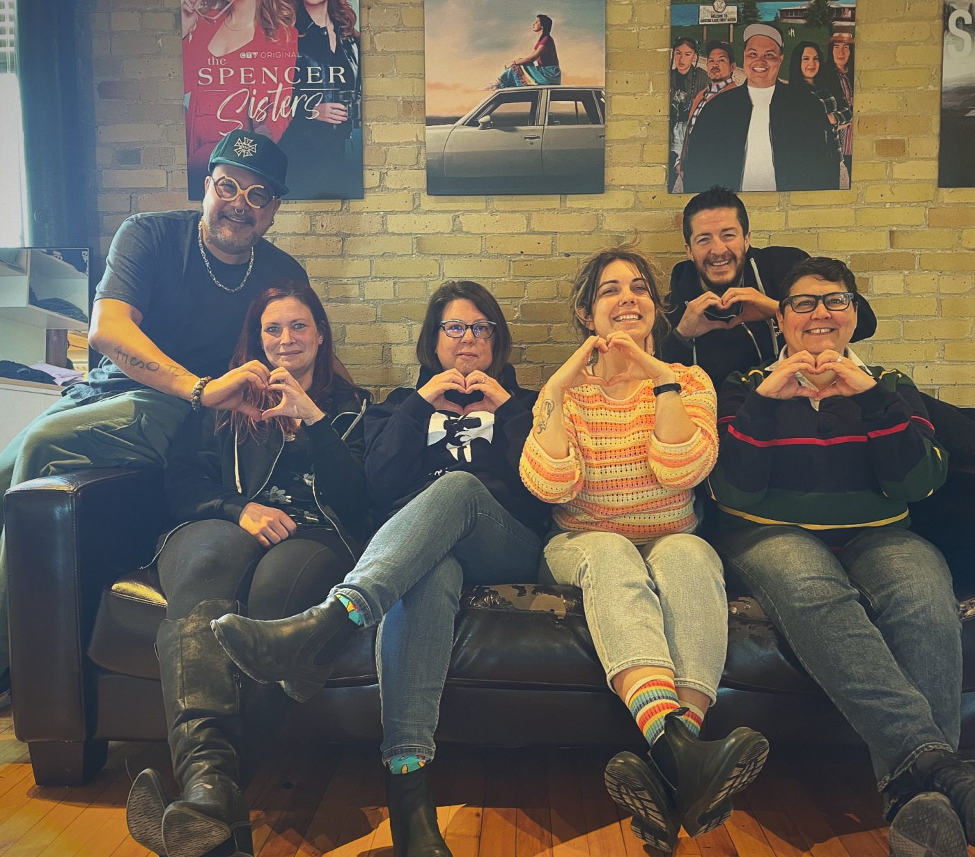 Six people sitting on a couch making heart symbols with their hands